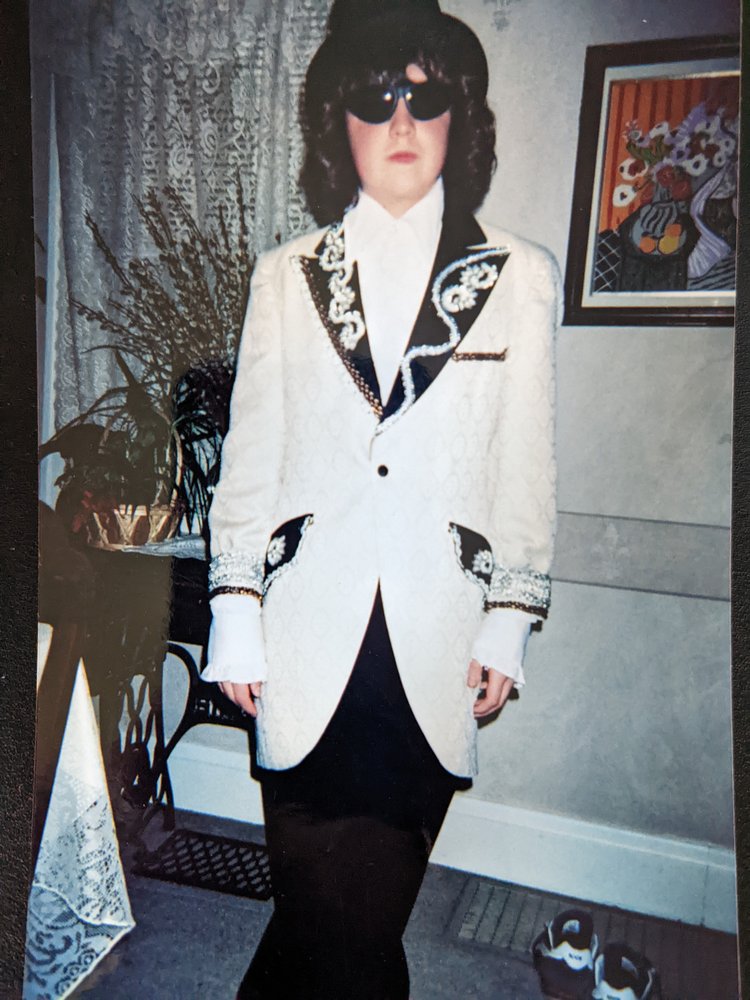 Middle school Ben dressed in a white suit, sunglasses, and a dark wig for an 8th grade limo ride.